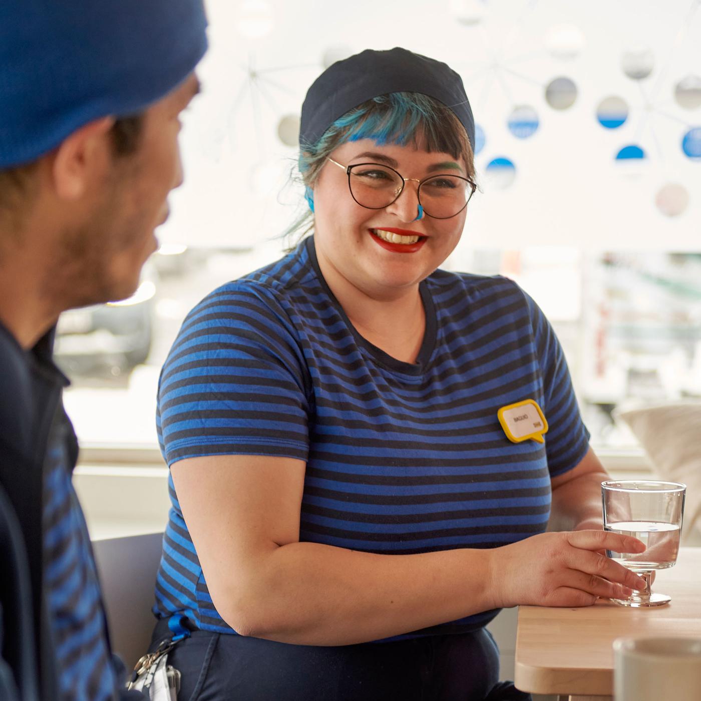 To IKEA medarbejdere, en med blåt hår, nyder et glas vand i personalekantinen.