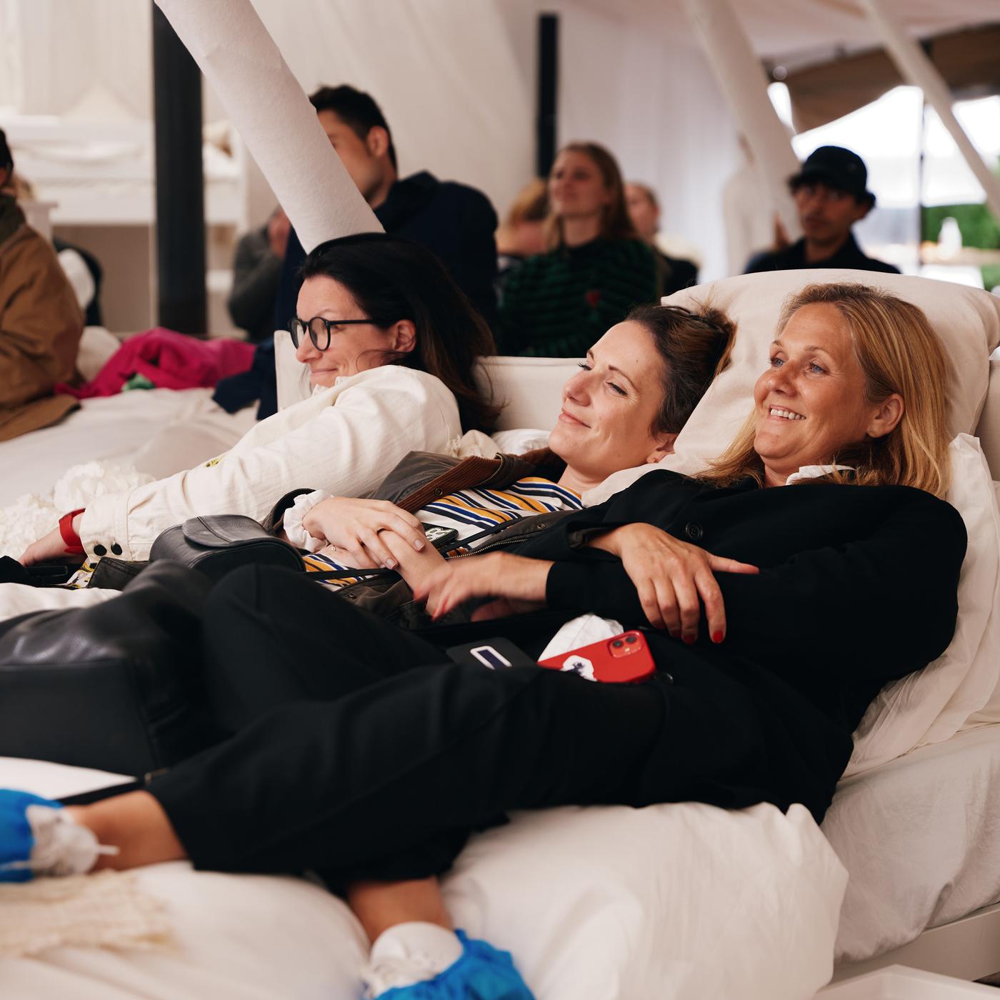 To kvinder ligger i en hvid stol med overtøj på, mens de lytter til noget.