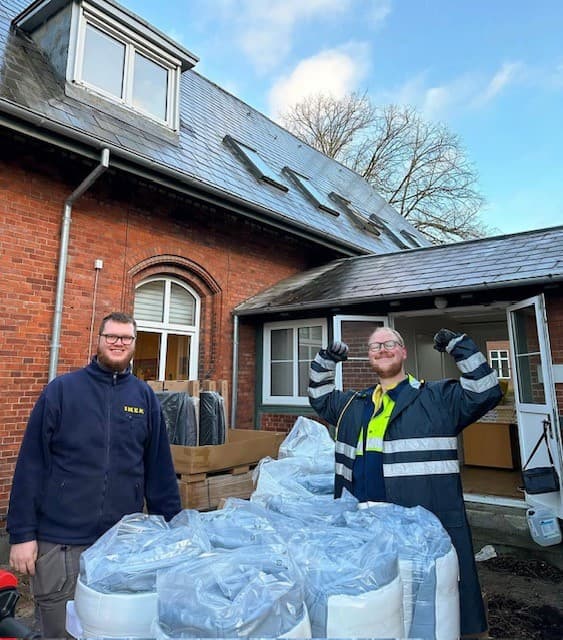 To mænd står foran Kirkens Korshærs herberg i Odense den ene løfter armene i vejret og viser muskler mens den anden smiler foran dem står en masse madrasser rullet pænt sammen i poser klar til at blive doneret.