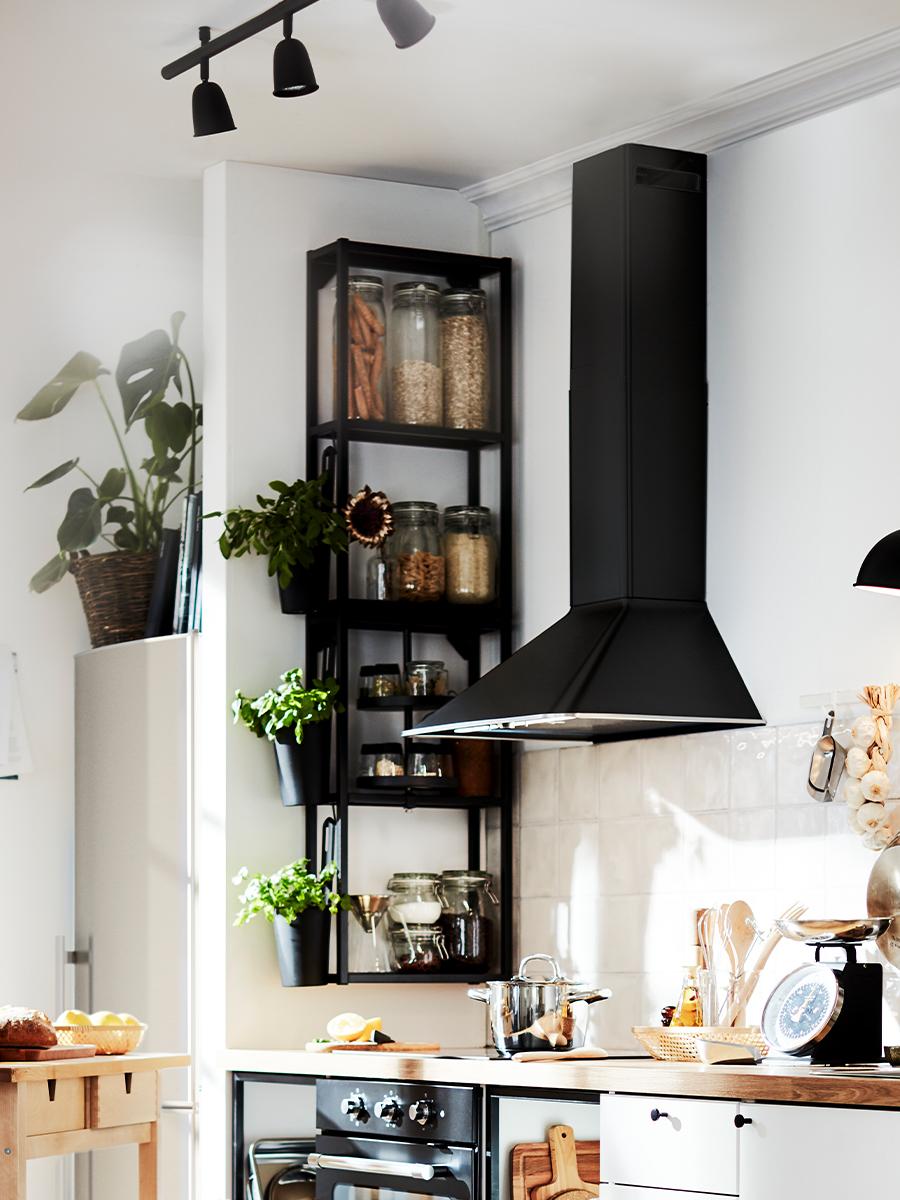 To svarte ENHET veggoppbevaring med hyller montert på en hjørnevegg på kjøkkenet, ved siden av en svart veggmontert ventilator.