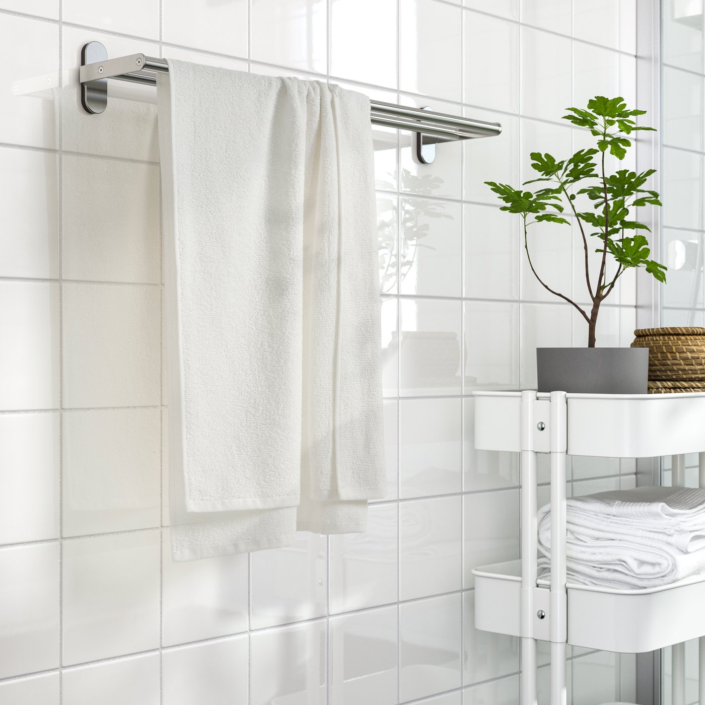 Toalla blanca LUDDVIAL colgando en un baño blanco junto a carrito blanco.