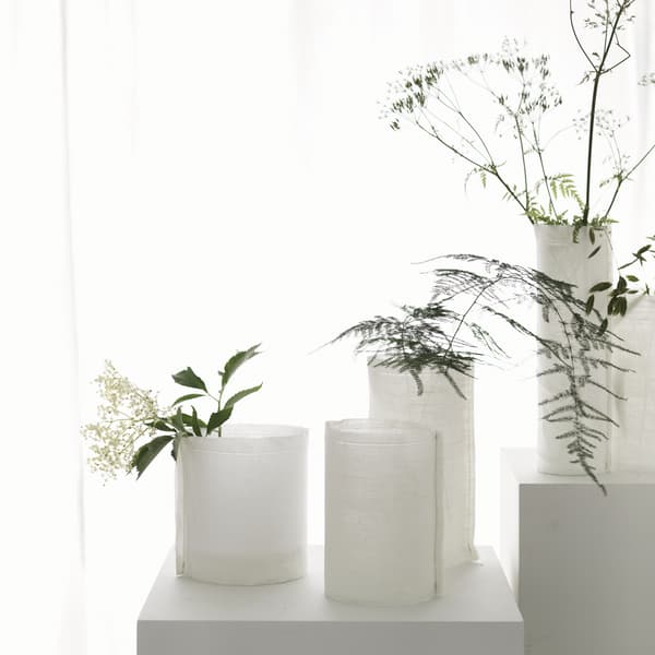 Több különböző méretű, fehér anyaggal bevont, köralakú vázában egy-egy szál zöld növény.