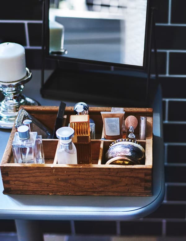 Toiletries organised in a small wooden box in a black tiled bathroom.