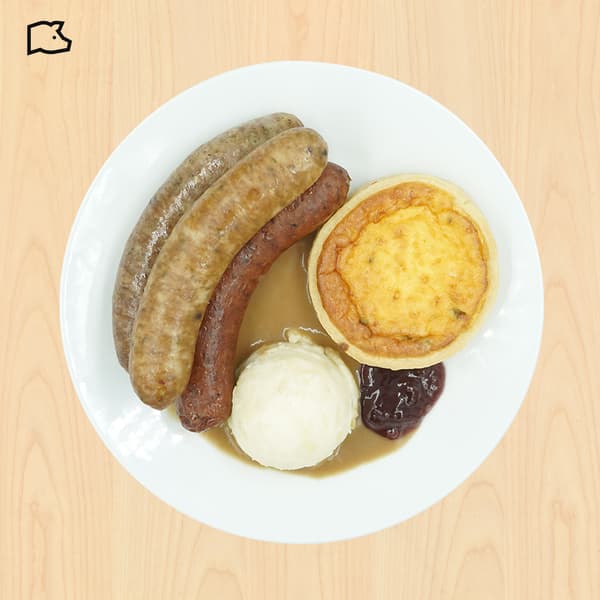 Top-down view of a hearty plate with three sausages, mashed potatoes, gravy, savory pie, and dark chutney on a white dish.