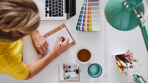 Top-down view of a person sketching at a desk with color swatches laptop coffee and design tools.