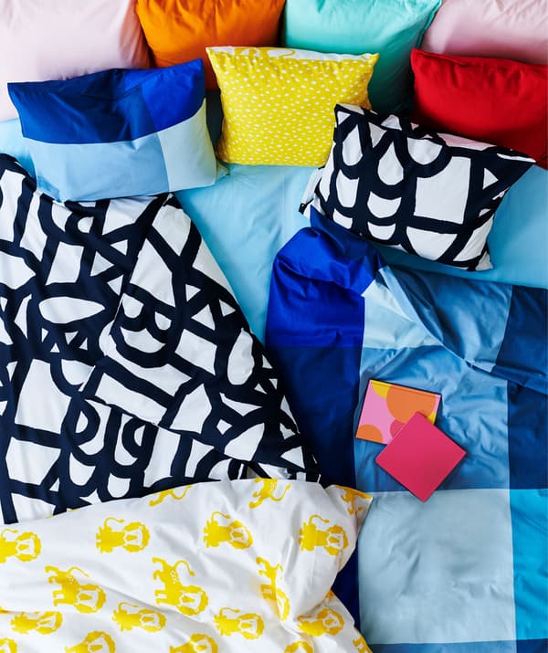 Top of a bed covered with a rich mix of sharply colored and patterned duvets, cushions and textiles.