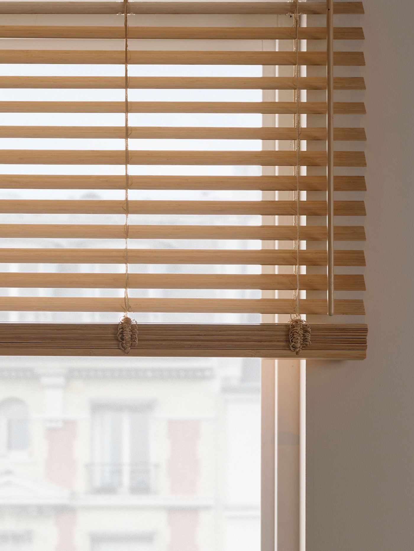 Träfärgade rumsmörkande persienner monterade i ett fönster, med stadsvy i bakgrunden.