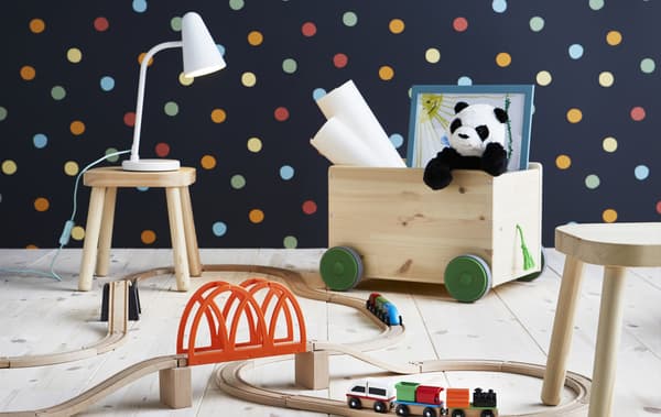 Train, rangement pour jouets à roulettes et tabourets en bois dans une pièce au mur à pois.