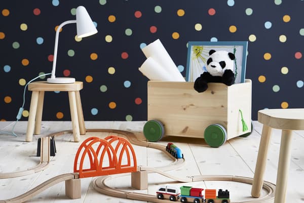 Train, rangement pour jouets à roulettes et tabourets en bois dans une pièce au mur à pois.