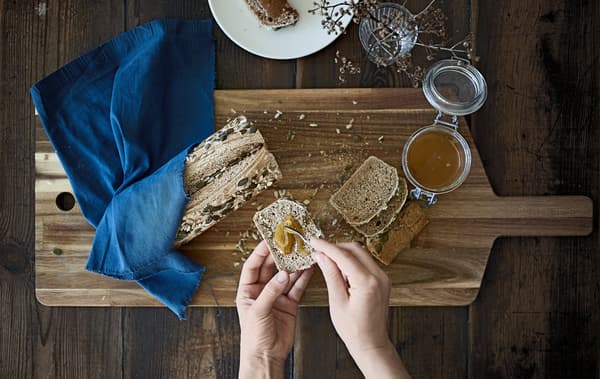 Tranche de pain aux graines et pot de miel, sur une planche en bois.