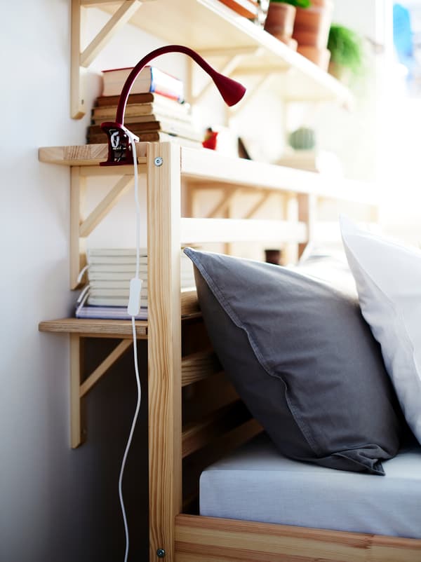TRANHULT/SANDSHULT shelves fill the space between a wall and a bed, creating a combination of storage and bedside table.