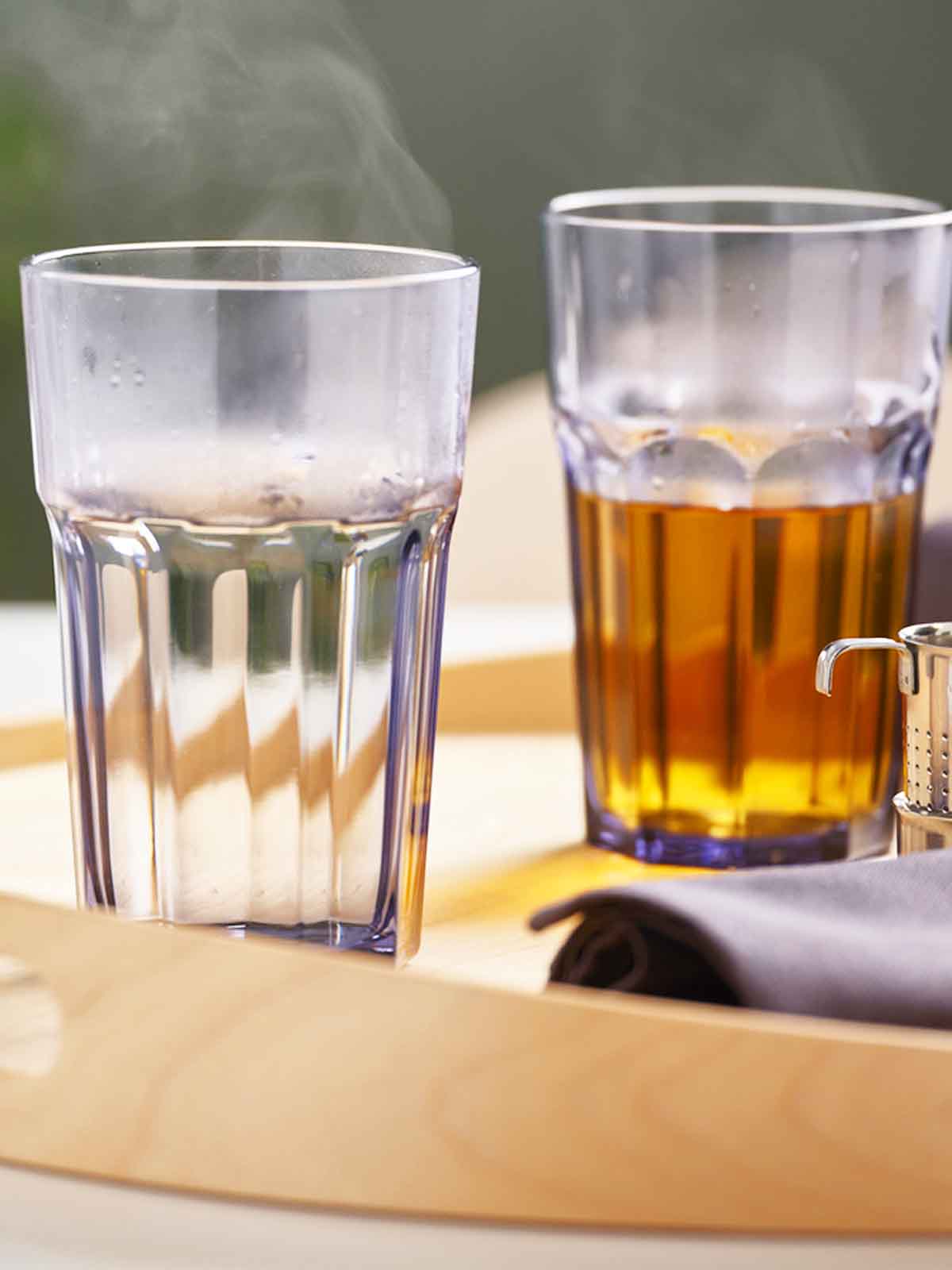 Transparent glass POKAL glasses filled with hot drinks on a wooden tray.