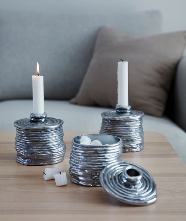 Tre candelieri metallici, due con una candela e un terzo con il coperchio aperto, per mostrare il piccolo contenitore al suo interno - IKEA