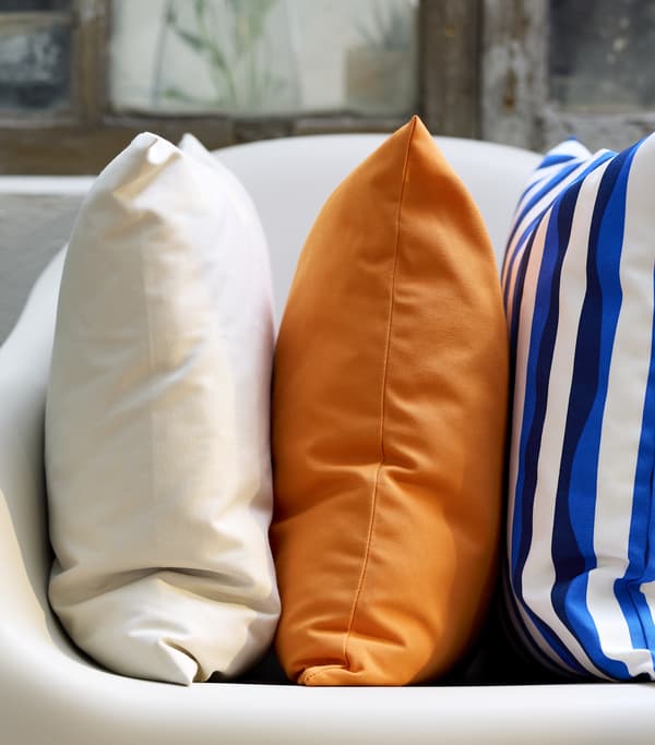Tre cuscini colorati uno bianco, uno arancione e uno a righe bianche e blu