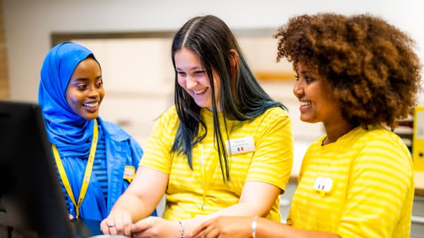 Tre dipendenti in divisa IKEA lavorano insieme al computer e discutono con espressione concentrata del loro lavoro in un ambiente luminoso e moderno.