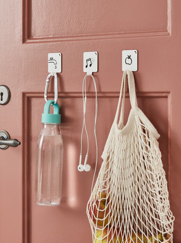 Tre ganci autoadesivi PLUTT bianchi applicati a una porta e decorati con disegni a pennarello nero che rappresentano gli oggetti da appendere.