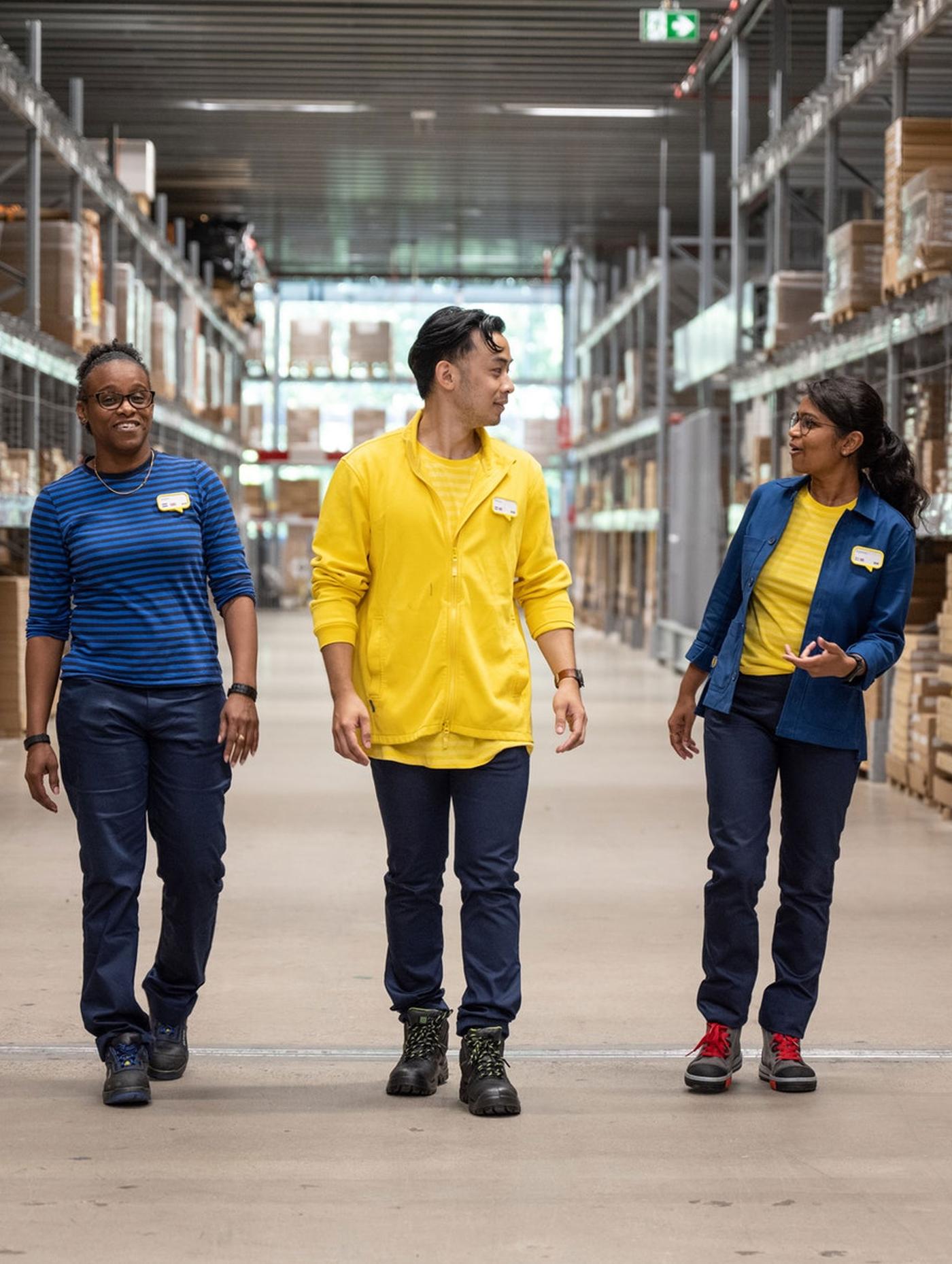 Tre IKEA ansatte går mens de prater mellom reolene på selvbetjeningslageret.