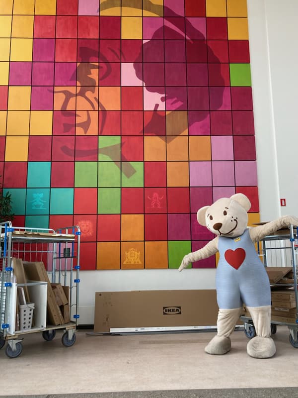 Tre IKEA medarbejdere står endt mod kameraet og skubber tre vågne med IKEA møbel pakker ind af hovedbygningen hos OUH skolen også kendt som H C Andersen Børne og ungehospital.
