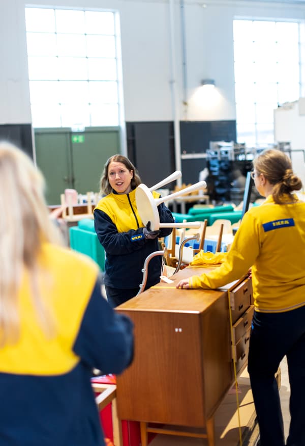 Tre IKEA-medarbetare som pratar vid en begagnad skänk i trä