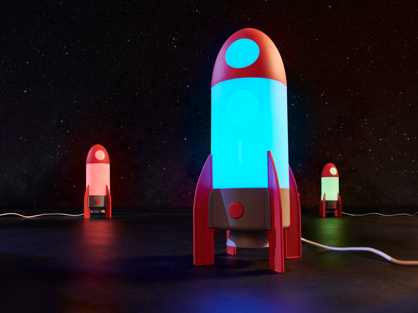 Tre lampor i form av en rymdraket står i ett mörkt rum och lyser.