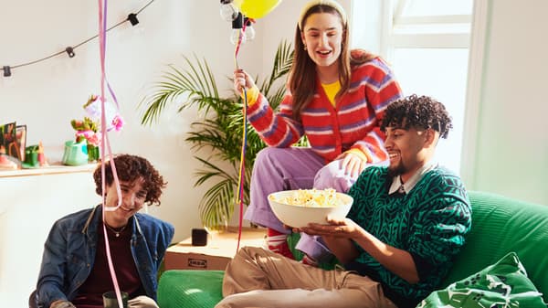 Tre persone sedute su e intorno a un divano verde che festeggiano quello che sembra essere un compleanno. Il ragazzo seduto sul divano ha in mano una ciotola di popcorn.