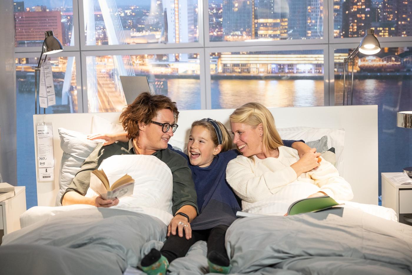 Tre personer i en säng som läser en bok och skrattar