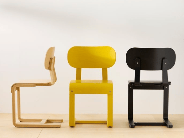 Tre stolar står uppradade mot en vit vägg. Två stolar är gula och en svart.