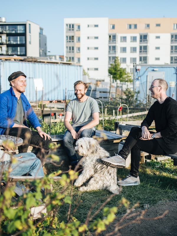 Tre uomini seduti mentre parlano in un orto in centro città. Al centro, c'è anche un cane.