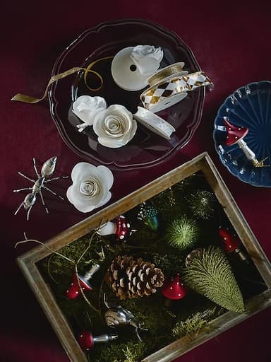 Tree decorations and ribbon in bowls and boxes on a table.