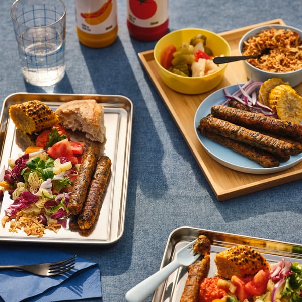Tres bandejas con platos a de verduras y salchichas a base de vegetales KORVMOJ, sobre una superficie con un mantel azul piedra opaco. 