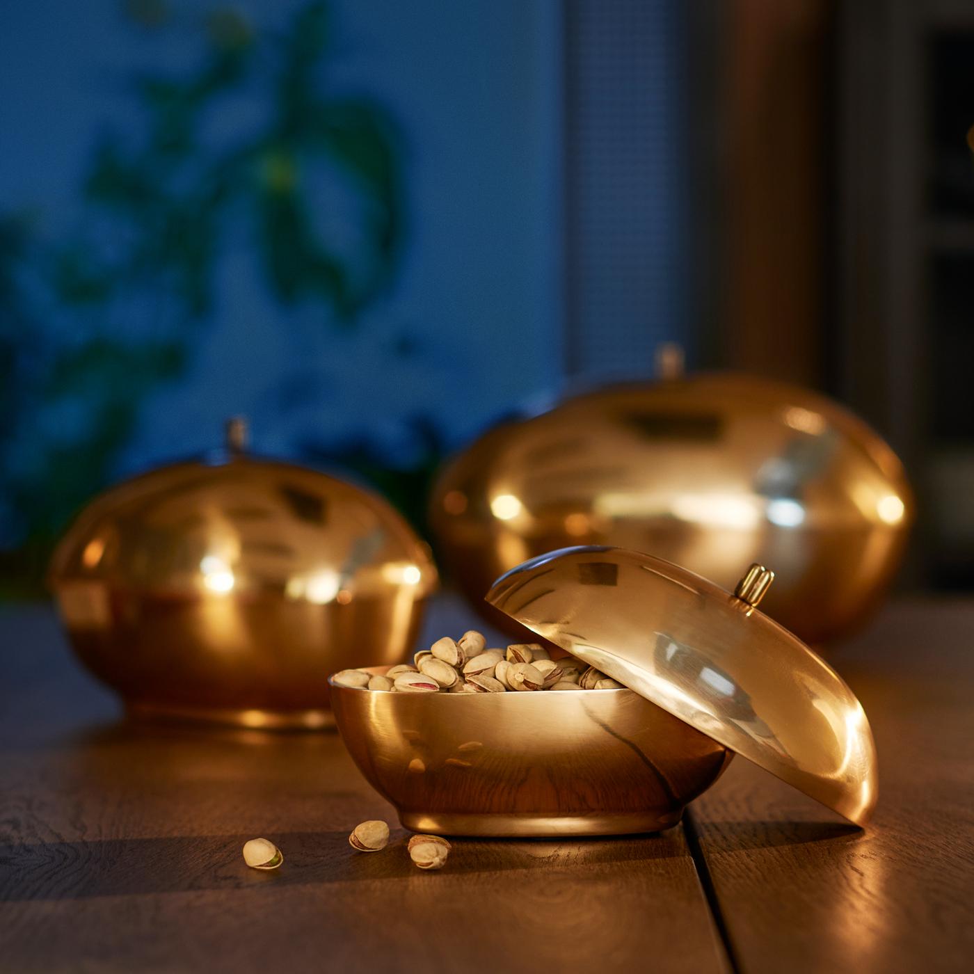 Tres boles GOKVÄLLÅ, uno de ellos está lleno de pistachos y tiene la tapa inclinada y apoyada en el borde.