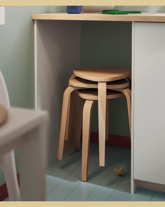 Tres butacos de madera IKEA apilados uno sobre otro bajo un mesón de cocina.