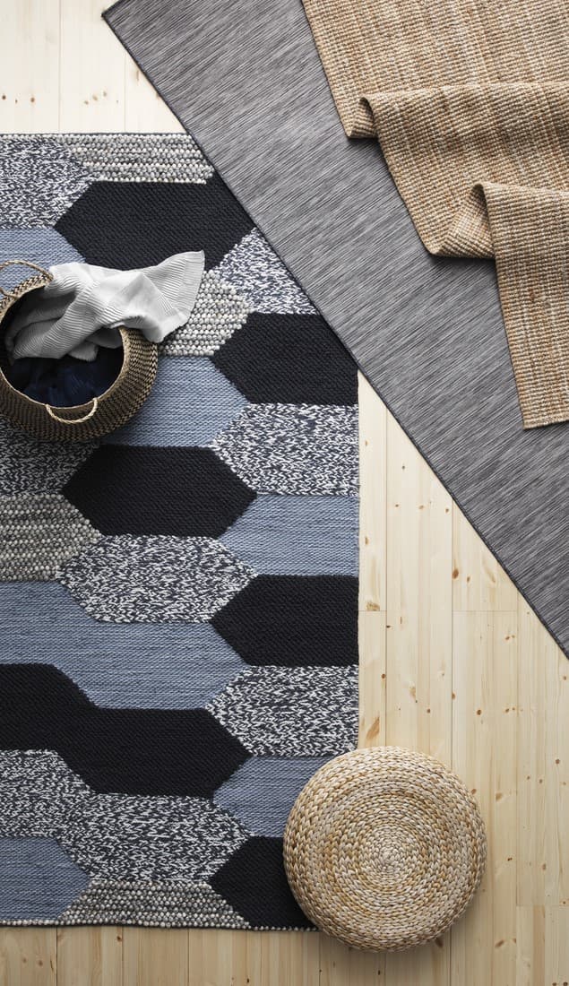 Tres distintas alfombras sobre un piso de madera. Una e las alfombras tiene diseños y las otras dos son lisas, una gris y la otra café