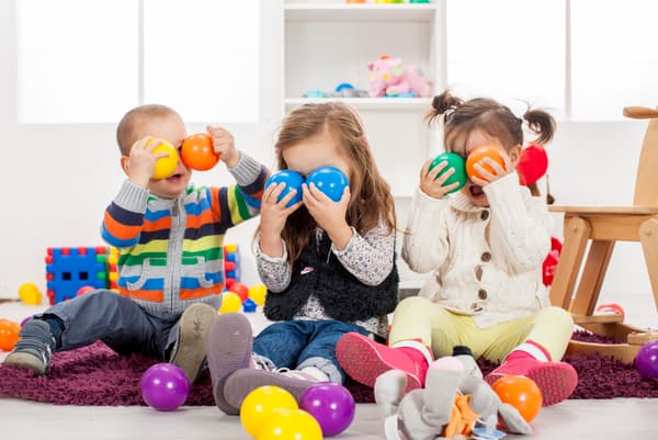 Tres niños jugando con pelotas plásticas en una pieza que contiene otros juguetes IKEA.