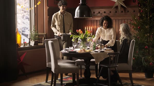 Tres personas se reúnen alrededor de una mesa redonda INGATORP decorada con flores frescas para comer juntos una comida navideña.