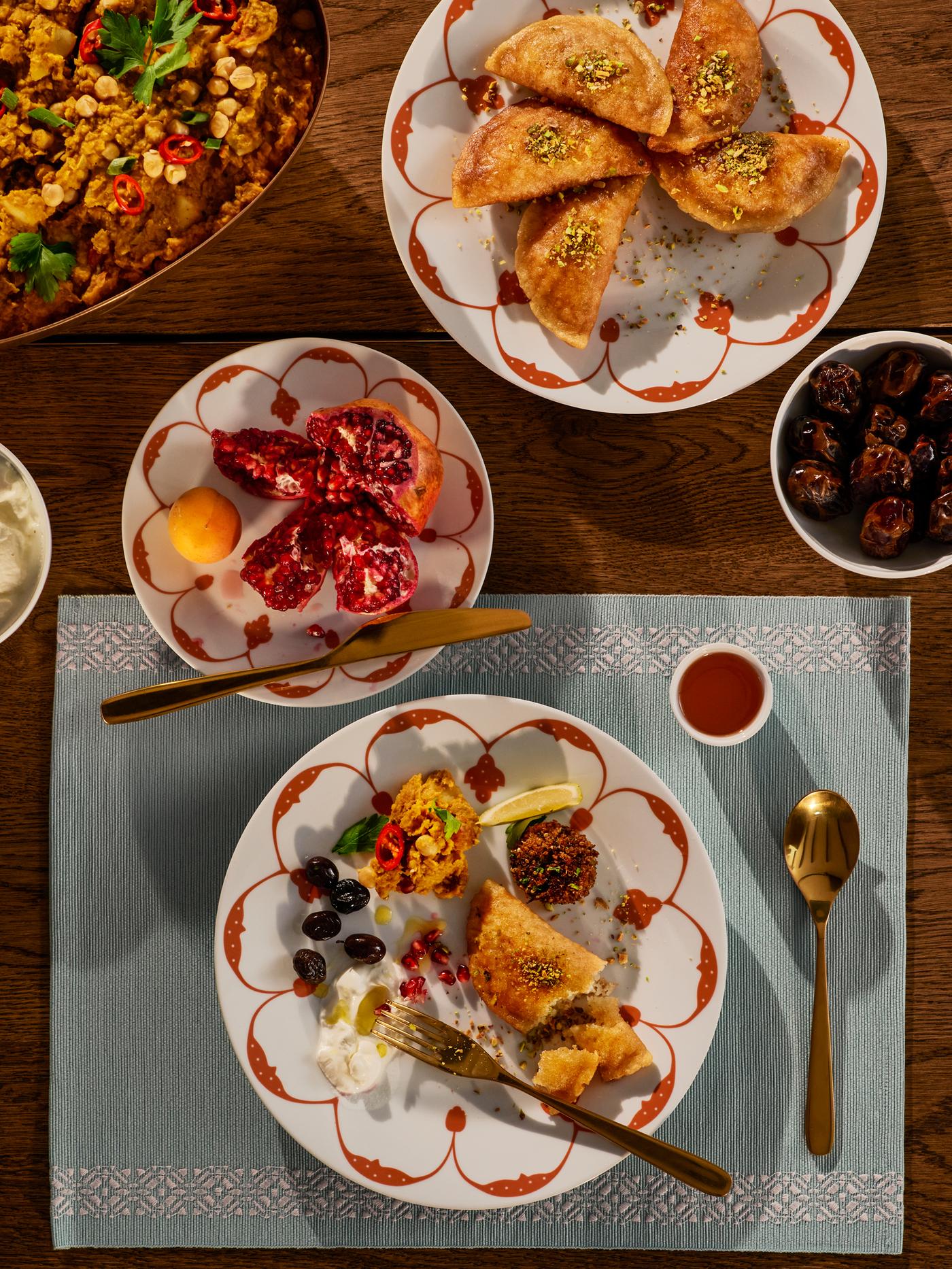 Tres platos GOKVÄLLÅ con comida festiva y un cuenco GOKVÄLLÅ lleno de dátiles colocados sobre un mantel individual GOKVÄLLÅ.