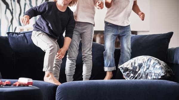 Tres rapaces descalzos saltando nun sofá IKEA azul.