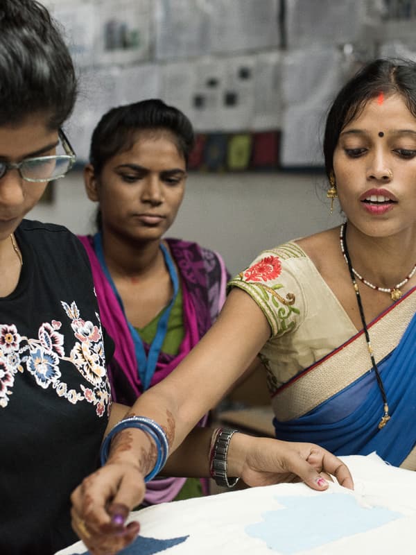 Tres tejedoras indias con trajes tradicionales discuten el diseño de un tapete.
