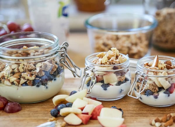 Tres xarros de vidro con iogur, granola, froita fresca e noces nun mesado de madeira.