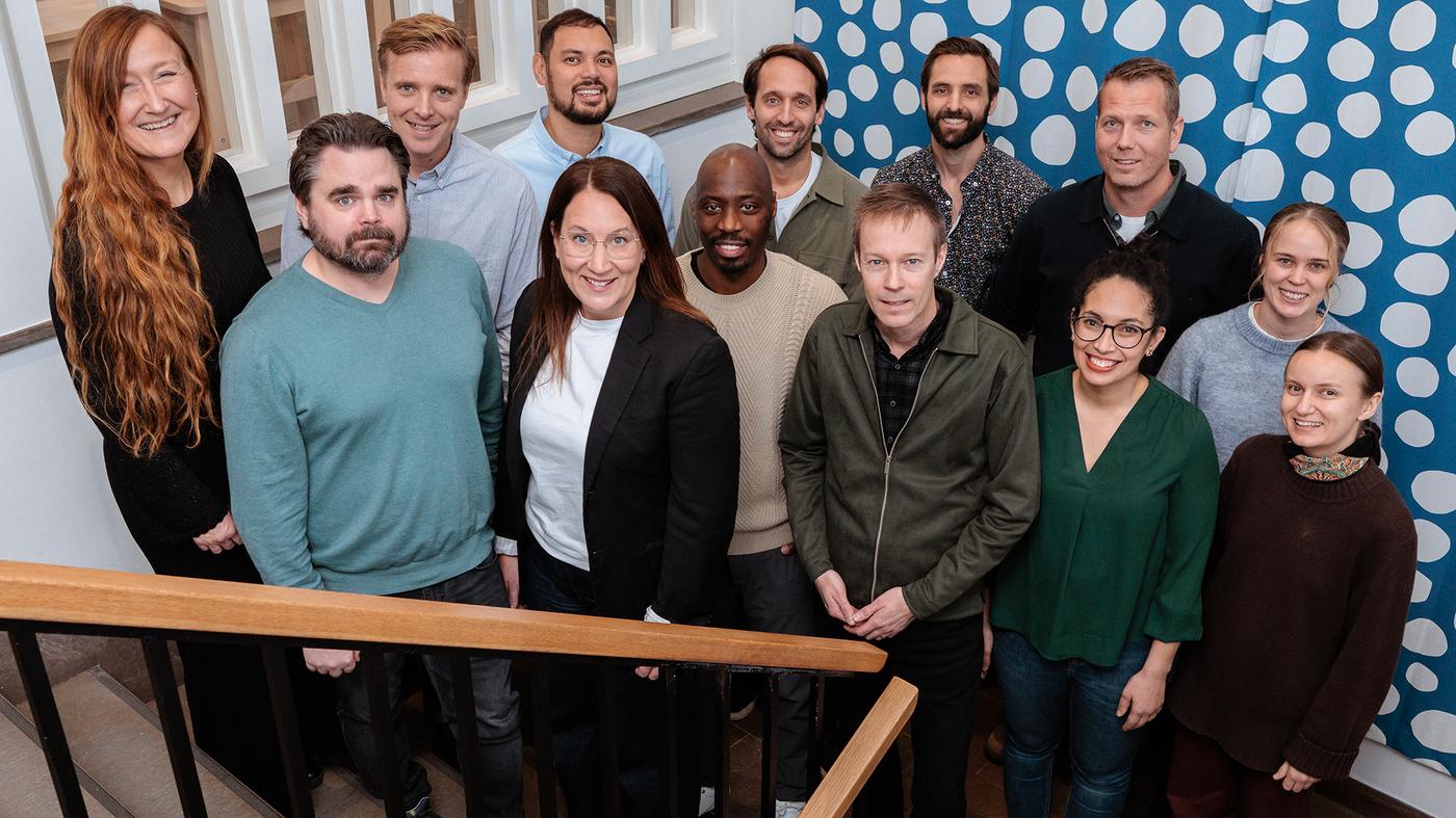 Tretton personer står i en trappa. Väggen är blå- och vitprickig. 