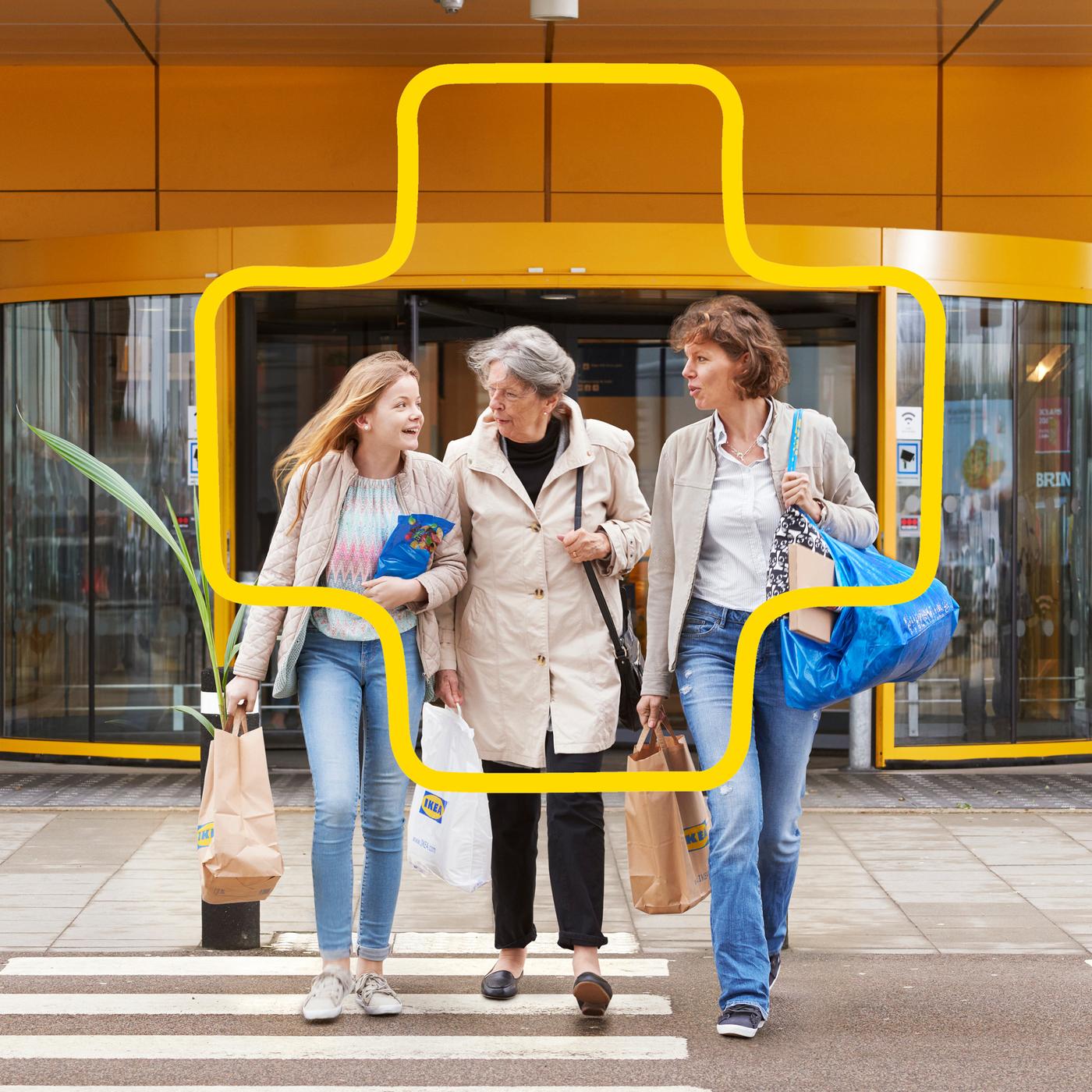 Tri osobe prelaze pješački prijelaz ispred robne kuće, noseći vrećice s namirnicama.