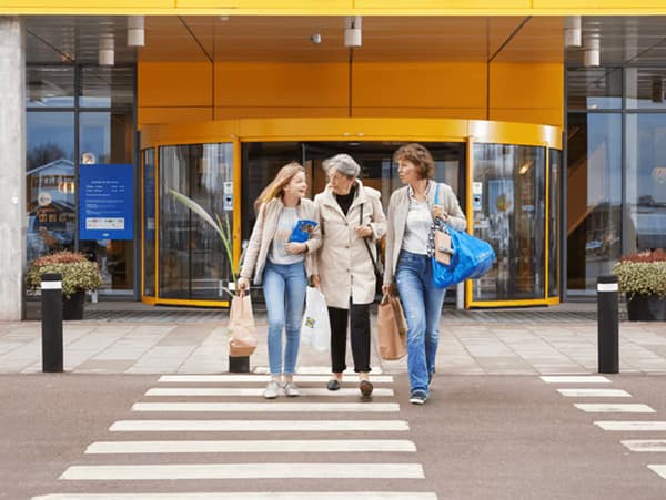 Tri osobe prelaze prešački prelaz ispred robne kuće IKEA.