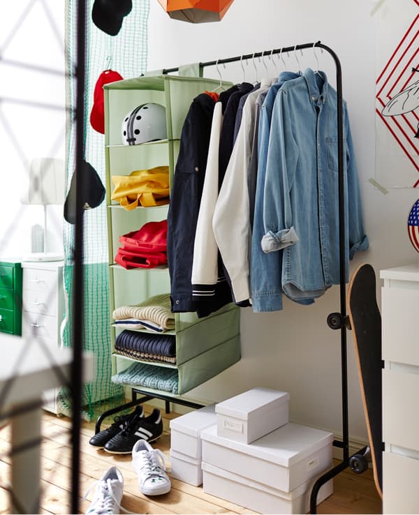 Tringle à habits avec chemises sur cintres et organiseur à suspendre. En dessous, quelques boîtes pour les chaussures.