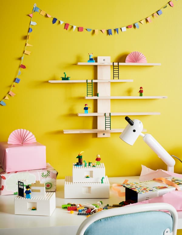 Trois boîtes BYGGLEK blanches sur le bureau d’un enfant soutenant des figurines miniatures LEGO, et des briques LEGO sont éparpillées autour.