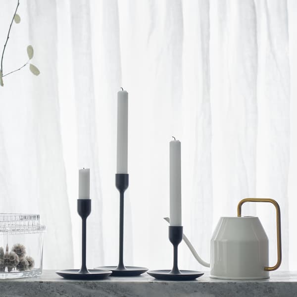 Trois bougeoirs noirs de différentes hauteurs sur fond blanc, avec arrosoir et bocaux en verre.