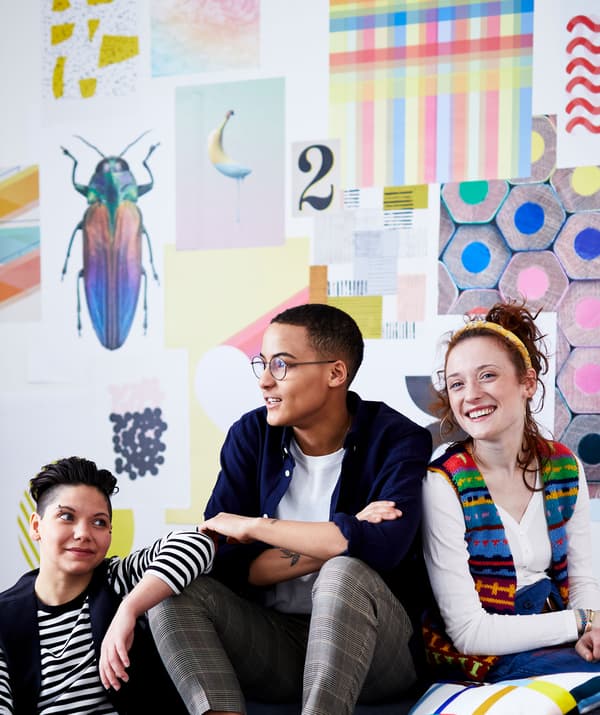 Trois colocataires assis contre un mur revêtu d'images multicolores.