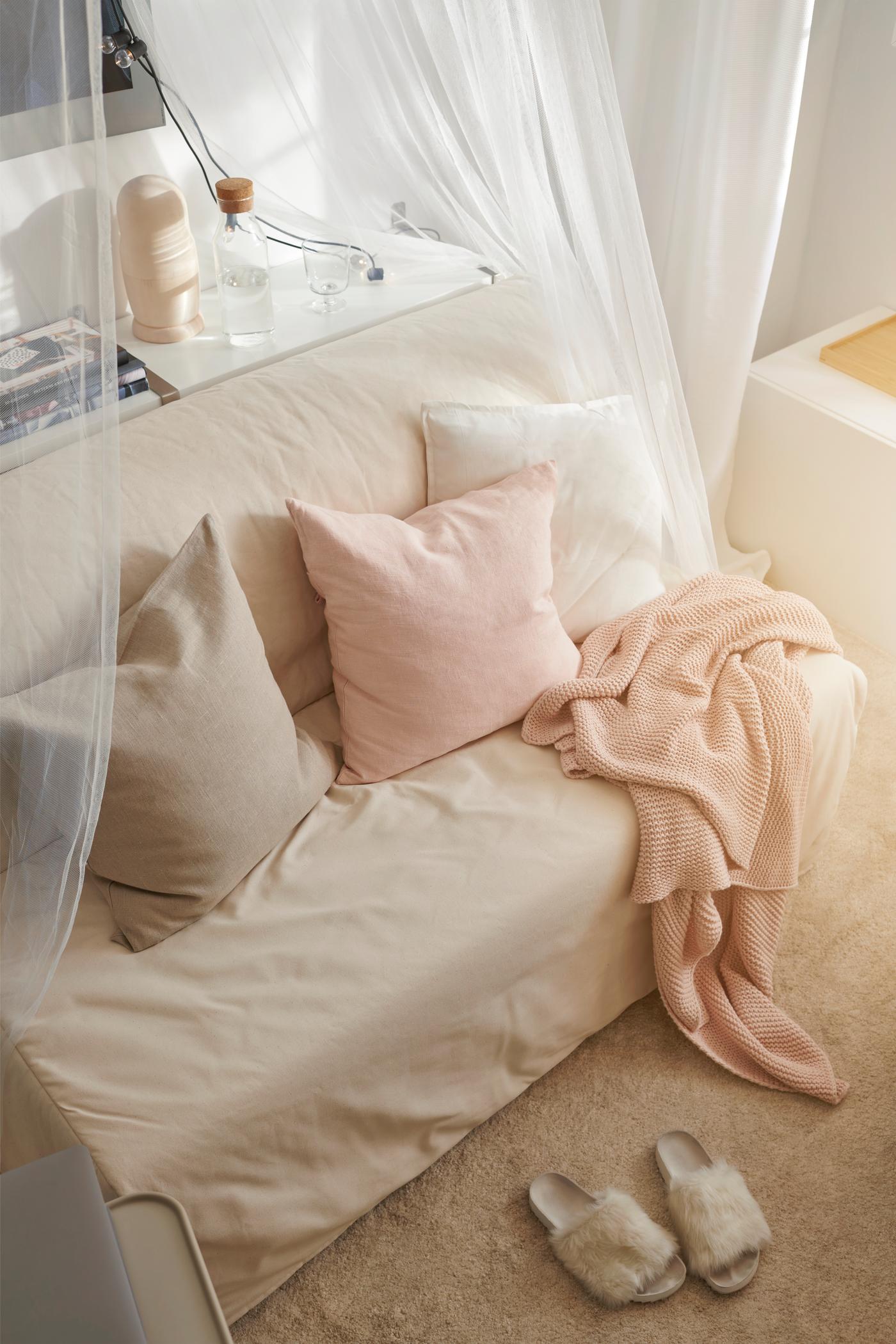 Trois coussins sur un convertible LYCKSELE HÅVET. Plaid rose jeté dessus. De la gaze enveloppe le convertible.