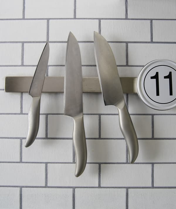Trois couteaux accrochés à un rail magnétique sur un mur carrelé.