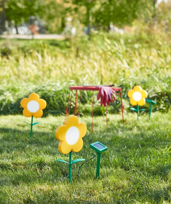 Trois fleurs/bornes à énergie solaire à LED pour l’extérieur jaunes sur une pelouse, en été.