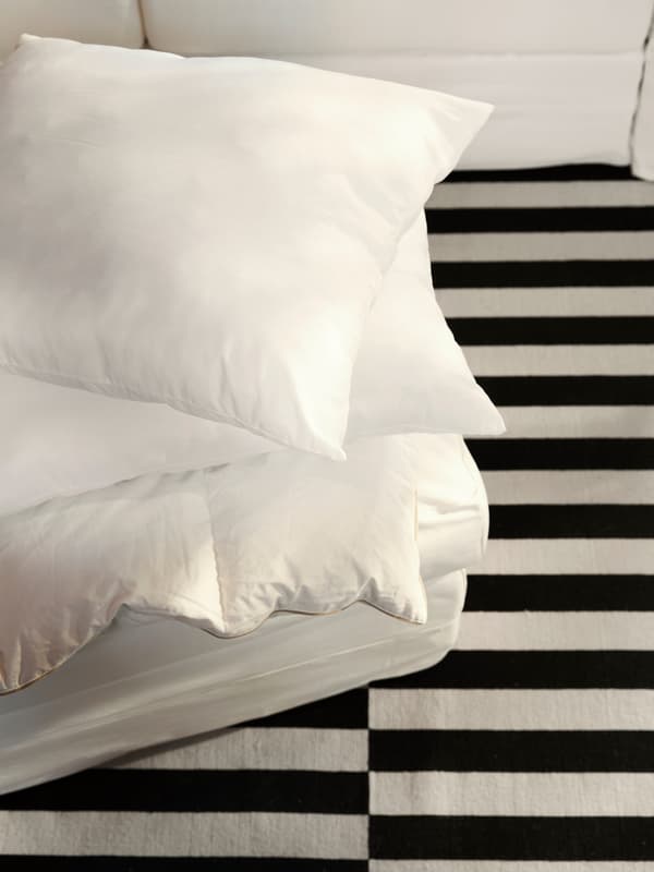 Trois oreillers LAPPTÅTEL et un coussin de canapé GRÖNLID couleur crème, empilés sur un tapis STOCKHOLM rayé.
